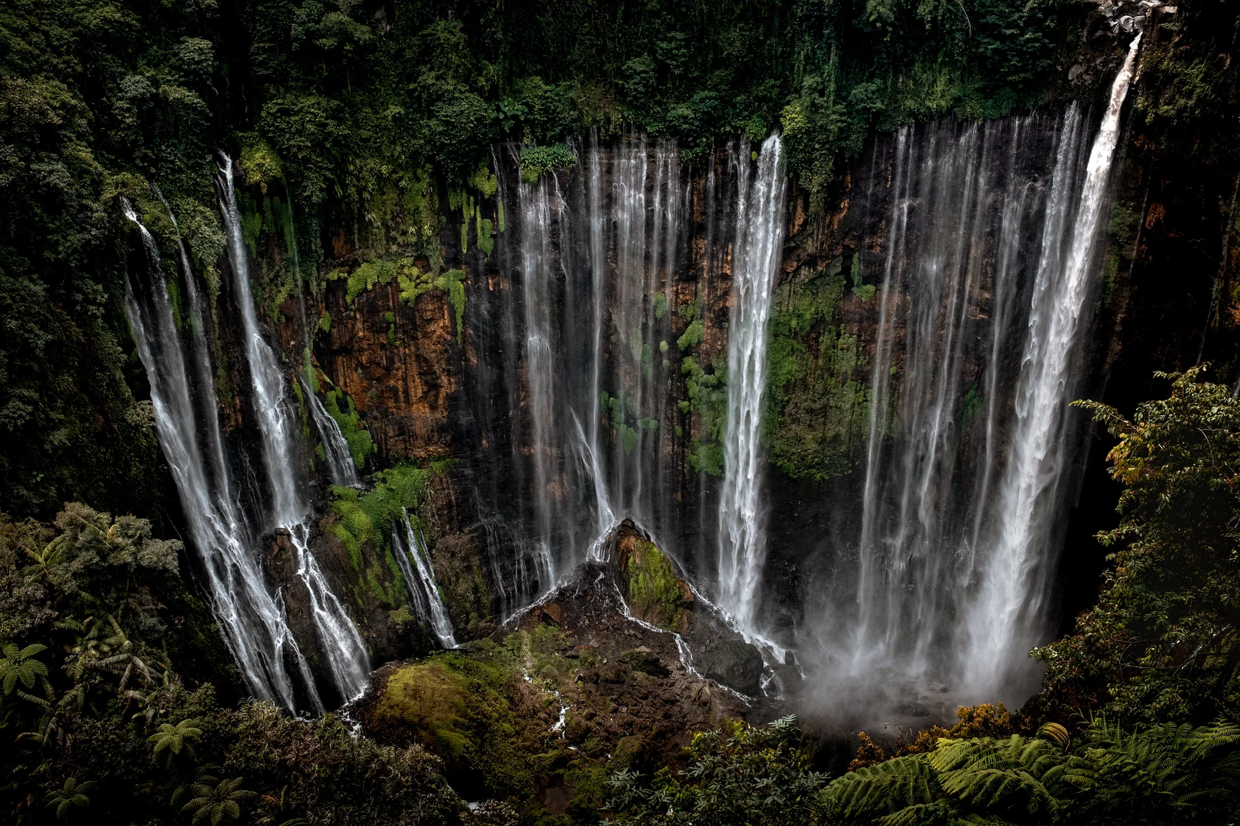 Panorama lebar Tumpak Sewu dengan deretan air jatuh di tebing hijau